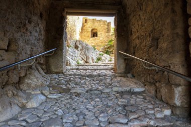 View through a dark stone gate to ruins of the ancient Greek city of Acrocorinth with stone walls. Greece.