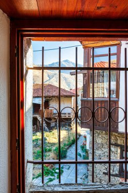 A view through a traditional wooden-framed window in Elati, Trikala, Greece, showcasing the village's stone houses and tiled rooftops with mountainous scenery. clipart