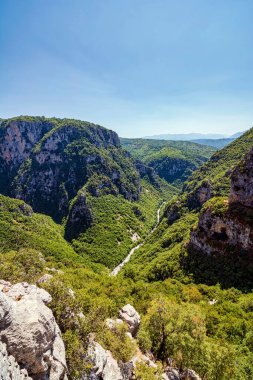 Spectacular aerial view of Vikos Gorge in Zagori, Greece, showcasing steep rocky cliffs and lush green valleys under a clear sky. clipart