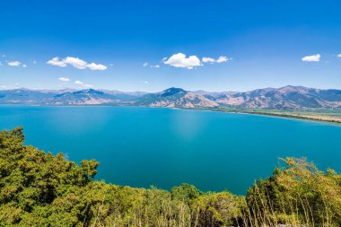 Kuzey Makedonya, Arnavutluk ve Yunanistan 'ın üç noktasında yer alan ve dağlarla çevrili olan Prespa Gölü' nün panoramik manzarası ve berrak mavi su.