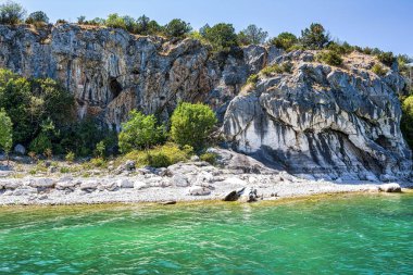 Yunanistan 'daki Megali Prespa Gölü' nün kayalık kıyı şeridinde doğal kayalıklar ve yeşilliklerle çevrili antik dini kaya resimleri yer alıyor..