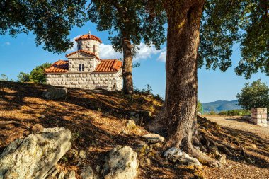 Yunanistan 'ın Maniaki kentinde büyük ağaçların ve kayalık arazilerin arasına yerleştirilmiş kırmızı kiremitli bir taş kilise, huzurlu doğal ve mimari güzellikleri yakalıyor..
