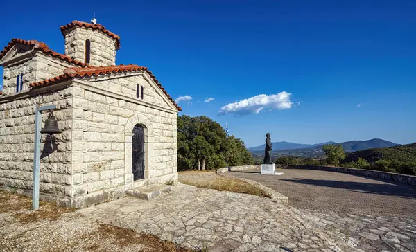 Yunan bağımsızlık kahramanı Papaflessas 'ın taş bir şapel ve heykeli, açık mavi gökyüzü altındaki manzaralı bir dağ manzarasına bakan Yunanistan' ın Maniaki kentindeki bir tepede duruyor..