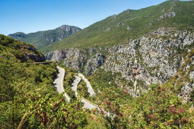 A winding mountain road along Route 82 offers stunning views of the rugged Nedontas Gorge in the Peloponnese, Greece, surrounded by lush greenery. clipart