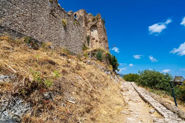 Yunanistan 'ın Mystras kentinden antik taş kale duvarları, ortaçağ mimarisi ve tepenin yamacında manzaralı bir kaldırım yolu sergiliyor..