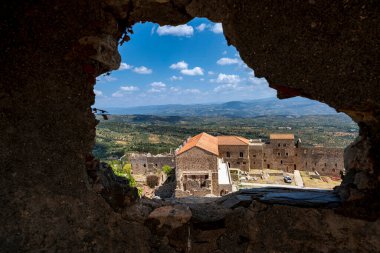 A unique view of the Palace of the Despots in Mystras, Greece, framed by a weathered hole in the ancient stone ruins. clipart