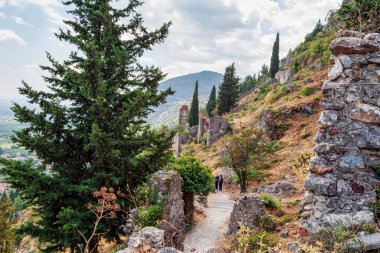 Yunanistan 'ın Mystras kentinin kalıntıları arasında sarmalanmış dingin bir patika, uzun selvi ağaçları ve tarihi yapılar manzarası var..