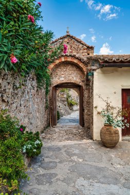 Charming arched entrance to Pantanassa Monastery in Mystras, surrounded by blooming flowers and traditional stone walls. clipart