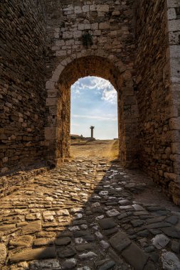 Methoni Kalesi 'ndeki tarihi taş kemer yolu, uzak bir sütun ve güneş ışığı çerçevesi, ortaçağ Yunan mimarisi ve tarihini vurguluyor.