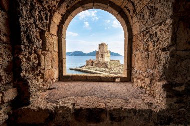 Denizi ve engebeli kıyı şeridini gören, Methoni Kalesi 'ndeki taş kemer deliğinden yapılmış Bourtzi kulesinin ikonik görüntüsü..