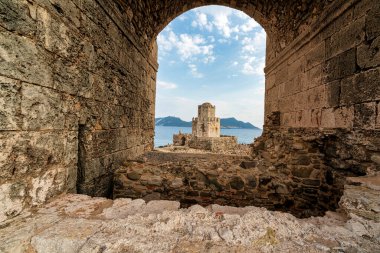 Denizi ve engebeli kıyı şeridini gören, Methoni Kalesi 'ndeki taş kemer deliğinden yapılmış Bourtzi kulesinin ikonik görüntüsü..