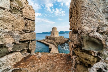 İyon Denizi ve kayalık kıyı şeridiyle çevrili taştan bir geçitle Methoni Kalesi 'ne bağlı ikonik Bourtzi Kulesi..