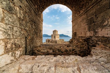 Denizi ve engebeli kıyı şeridini gören, Methoni Kalesi 'ndeki taş kemer deliğinden yapılmış Bourtzi kulesinin ikonik görüntüsü..