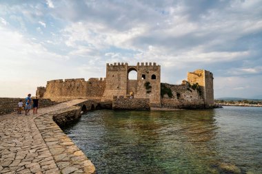 Methoni, Yunanistan - 25 Ağustos 2024: Methoni Kalesi 'nin ana kapısı, sakin sular üzerindeki taş bir köprüyle bağlanmış, ortaçağ Venedik işçiliğini vurguluyor.