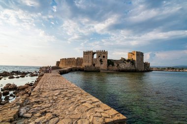 Methoni, Yunanistan - 25 Ağustos 2024: Methoni Kalesi 'nin ana kapısı, sakin sular üzerindeki taş bir köprüyle bağlanmış, ortaçağ Venedik işçiliğini vurguluyor.