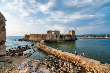 Methoni, Yunanistan - 25 Ağustos 2024: Methoni Kalesi 'nin ana kapısı, sakin sular üzerindeki taş bir köprüyle bağlanmış, ortaçağ Venedik işçiliğini vurguluyor.