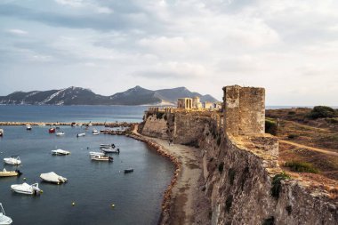 Methoni Kalesi 'nin sakin limana bakan kıyı duvarlarının çarpıcı manzarası. Arka planda demirlemiş tekneler ve manzaralı dağlar var..