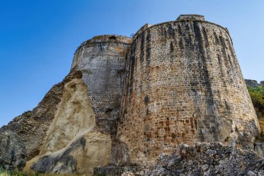 Koroni 'deki yıpranmış taş bir kuleye yakından bakın. Antik mimari, dokulu duvarlar ve yukarıda açık mavi gökyüzü sergileniyor..
