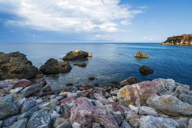 Koroni 'de sakin Akdeniz suları, dağınık kayalar ve bulutlu bir gökyüzünün altında sakin bir ufuk..