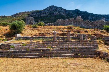 Yunanistan 'ın Messene kenti yakınlarındaki antik Arkadya Geçidi harabelerinde taş duvarlar, basamaklar ve berrak gökyüzü altında engebeli bir tepe manzarası yer alıyor..