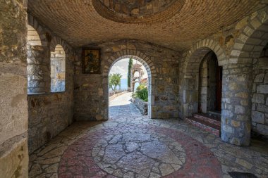 Yunanistan 'ın Mora kentindeki tarihi bir manastırın iç manzarası, taş kemerler, karmaşık döşemeler ve manzaralı bir açık hava manzarası yer alıyor..