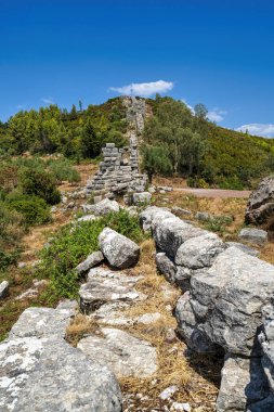 Yunanistan 'ın Messene kentinin antik duvarlarının taş kalıntıları, yemyeşil ve açık bir gökyüzünün altında yuvarlanan tepelerle çevrili..