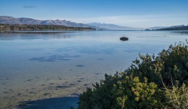 A partially submerged boat in the calm waters of Vourkari Wetland near Megara, Greece, reflecting the surrounding mountains under a clear sky. clipart