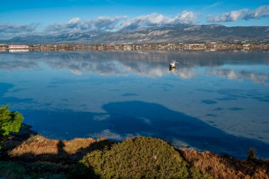 A tilted, partially sunken boat in the calm waters of Vourkari Wetland near Megara, Greece, reflecting mountains and sky in a serene landscape. clipart