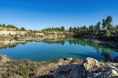 Yunanistan 'ın Evia kentinde terk edilmiş bir maden ocağında kayalık terasları ve dağınık yeşil çam ağaçlarını yansıtan manzaralı bir yapay göl oluştu..
