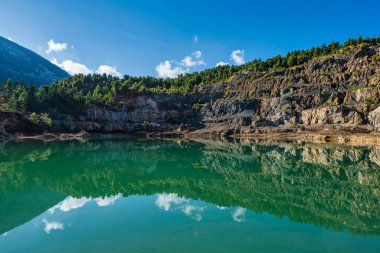 Yunanistan 'ın Evia kentindeki terk edilmiş bir taş ocağında huzurlu bir yapay göl kayalık uçurumları, gür çam ağaçları ve parlak mavi bir gökyüzünü yansıtıyor..