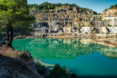Yunanistan 'ın Evia kentinde terk edilmiş bir maden ocağında kayalık terasları ve dağınık yeşil çam ağaçlarını yansıtan manzaralı bir yapay göl oluştu..