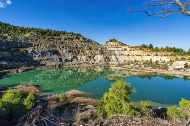 Yunanistan 'ın Evia kentinde terk edilmiş bir maden ocağında kayalık terasları ve dağınık yeşil çam ağaçlarını yansıtan manzaralı bir yapay göl oluştu..