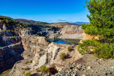 Yunanistan 'ın Evia kentindeki terk edilmiş bir taş ocağında, kayalık uçurumlar, seyrek bitki örtüsü ve uzak tepelerle çevrili çarpıcı bir yapay göl..