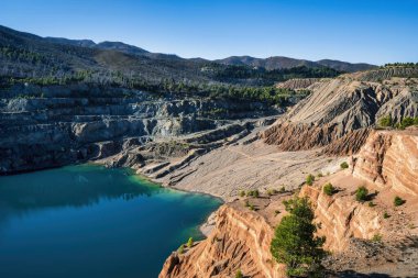 Yunanistan 'ın Evia kentindeki terk edilmiş bir taş ocağında bulunan derin mavi bir yapay göl, katmanlı kaya oluşumları, engebeli arazi ve ormanlı tepelerle çevrilidir..