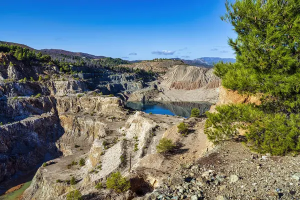 Yunanistan 'ın Evia kentindeki terk edilmiş bir taş ocağında, kayalık uçurumlar, seyrek bitki örtüsü ve uzak tepelerle çevrili çarpıcı bir yapay göl..