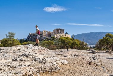 Atina, Yunanistan - 29 Eylül 2024: Yunanistan 'ın Atina kentindeki Areopagus Tepesi' nde tek başına dolaşan bir yolcu, açık mavi gökyüzü altındaki antik Akropolis 'e tepeden bakıyor.