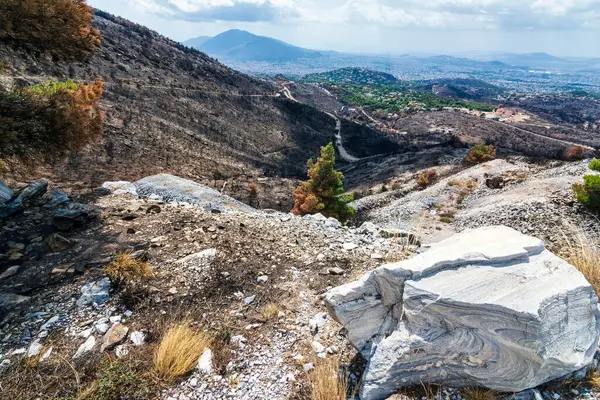 2024 'teki orman yangını felaketinin ardından Atina' ya bakan Penteli Dağı 'ndaki dağların içinden engebeli bir dağ yolu kıvrılıyor..