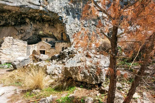 Penteli Dağı 'ndaki Davelis Mağarası' nın girişindeki taş şapel yangından zarar görmüş bitki örtüsü ve 2024 yangınından sonra dağılmış kayalarla çevrili..