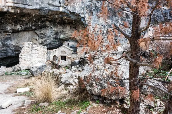 Penteli Dağı 'ndaki Davelis Mağarası' nın girişindeki taş şapel yangından zarar görmüş bitki örtüsü ve 2024 yangınından sonra dağılmış kayalarla çevrili..