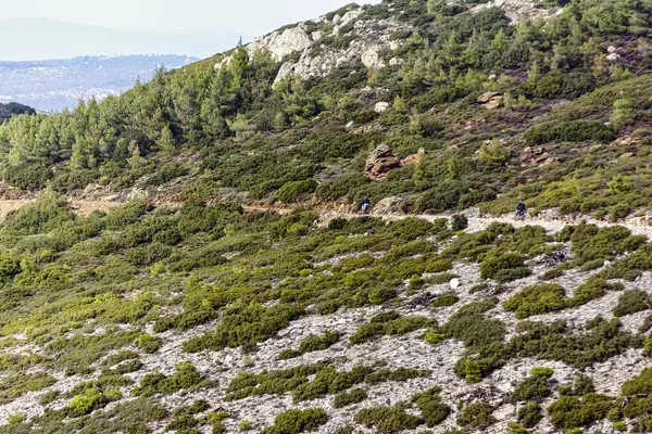 Atina 'nın dik bir Penteli yamacındaki kayalar ve çalılarla çevrili dar toprak patika boyunca giden iki bisikletçi..