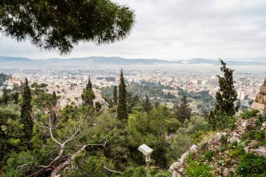 Areopagus Tepesi boyunca ağaçlar ve turistlerle Akropolis 'ten bakıldığında, Atina kentinin ortasında görünen antik Hephaestus Tapınağı.