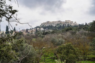 Akropolis, Antik Agora 'da sessiz bir noktadan yakalanan, ağaçlarla kaplı yamaçların arkasındaki Atina' nın siluetine hakim..