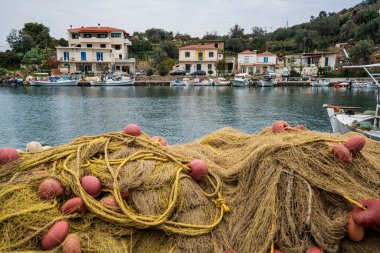 Methana, Yunanistan - 23 Mart 2025: Geleneksel balıkçı ağları Methana 'da sessiz bir Yunan limanının ön planında, arka planda tekneler ve rıhtım evleri bulunuyor.