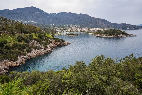 Methana yarımadasının panoramik manzarası, küçük bir liman, kayalık kıyı şeridi ve engebeli dağların desteklediği yemyeşil tepeleri gösteriyor..