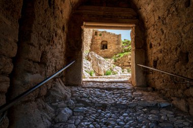 Akrokorinthos 'ta gölgeli bir taş geçidin içinden kayalık araziyi ve dışarıdaki güneş ışığıyla aydınlatılmış tarihi duvarları görün..