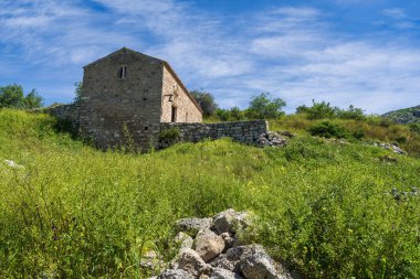 Akrokorinthos 'taki çimenli bir tepede küçük bir taş bina. Parlak, sakin bir gökyüzünün altında harabeler ve vahşi yeşilliklerle çevrili..