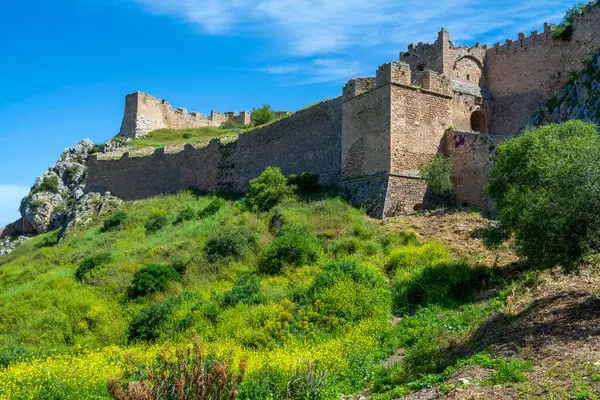 Akrokorinthos taş duvarlarının panoramik manzarası ve bahar bitkisinin üzerinde yükselen ortaçağ kuleleri.