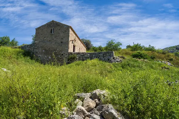 Akrokorinthos 'taki çimenli bir tepede küçük bir taş bina. Parlak, sakin bir gökyüzünün altında harabeler ve vahşi yeşilliklerle çevrili..