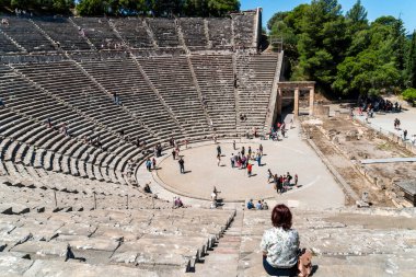 Epidaurus, Yunanistan - 11 Mayıs 2025: Turistler, MÖ 4. yüzyıl Yunan mimarisinin akustiği ve klasik tasarımı ile ünlü bir harikası olan Epidaurus Antik Tiyatrosu 'nun sahne ve koltuklarını keşfediyorlar..