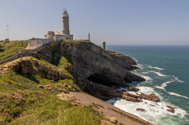 Santander, İspanya. Cabo Belediye Başkanı Deniz Feneri 'nin güneşli manzarası Biscay Körfezi' nin yukarısındaki uçurumlara tünemiş, kül taşı silindirik kuleyi saran kayalık sahil ve deniz manzarası